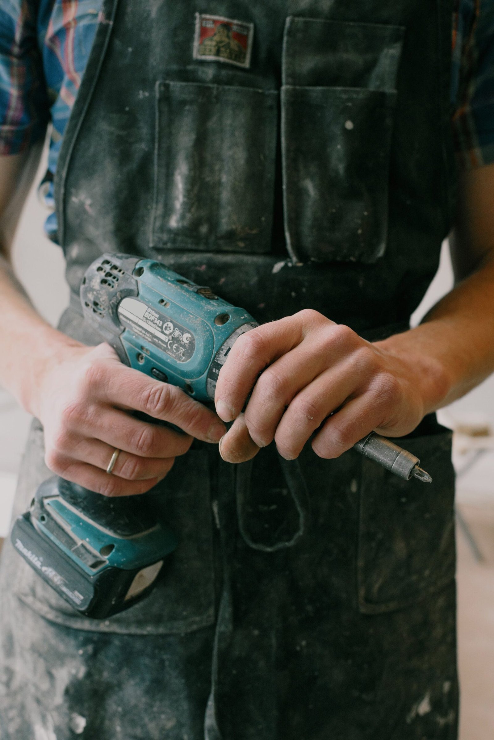 A man in overalls holding a drill, ready to work on a project.